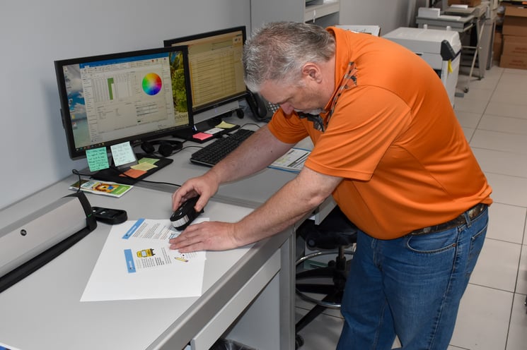 ohn Davis uses a special tool to inspect color values on pages from a From Drool to School book.