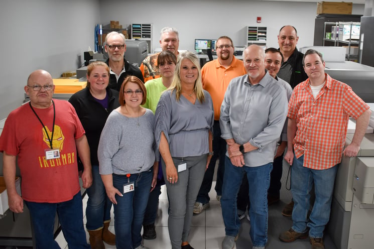 A group of people pose in a print shop.