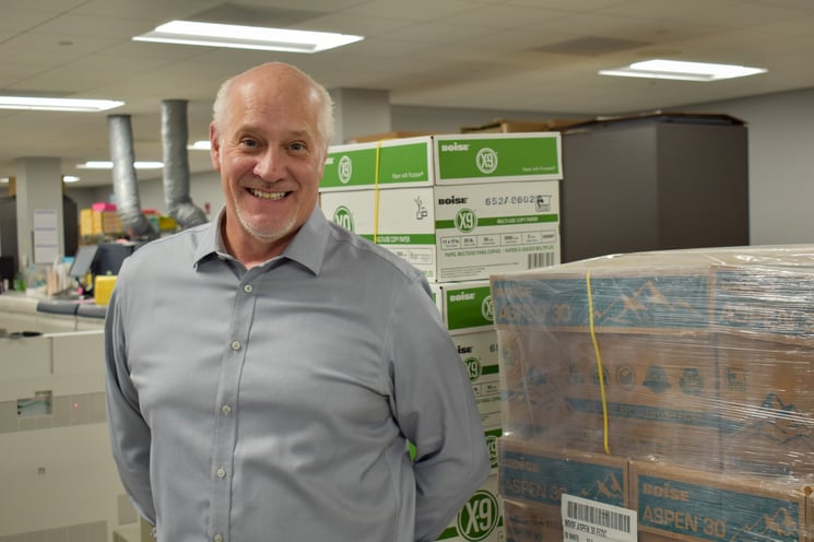 An older man poses in front of stacks of printer boxes.