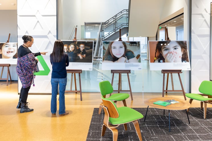 Two women with their backs to the camera examine a series of photos set on easels.