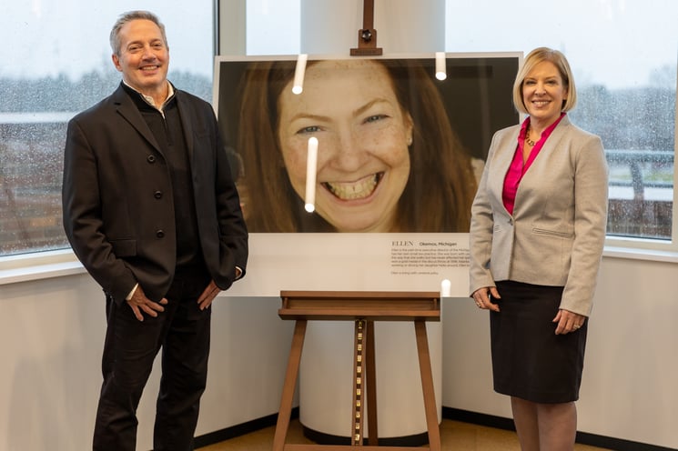 Photographer Rick Guidotti stands with Delta Dental Foundation Executive Director Holli Seabury in front of a large image depicting a smiling, middle-aged woman. The image sits on an easel.