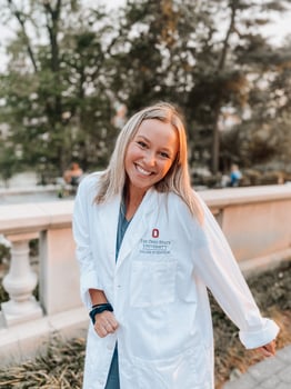 A portrait of a young woman with blonde hair smiling. She's wearing a white dentist's coat.