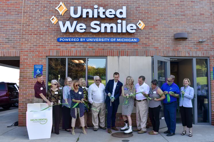 Group photo of people cutting a floss ribbon in front of a dental clinic.