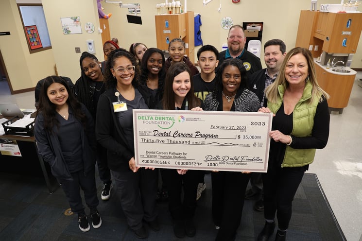 A group of students and teachers from the Walker Career Center stand in a group holding a giant check for $35,000 from the Delta Dental Foundation.