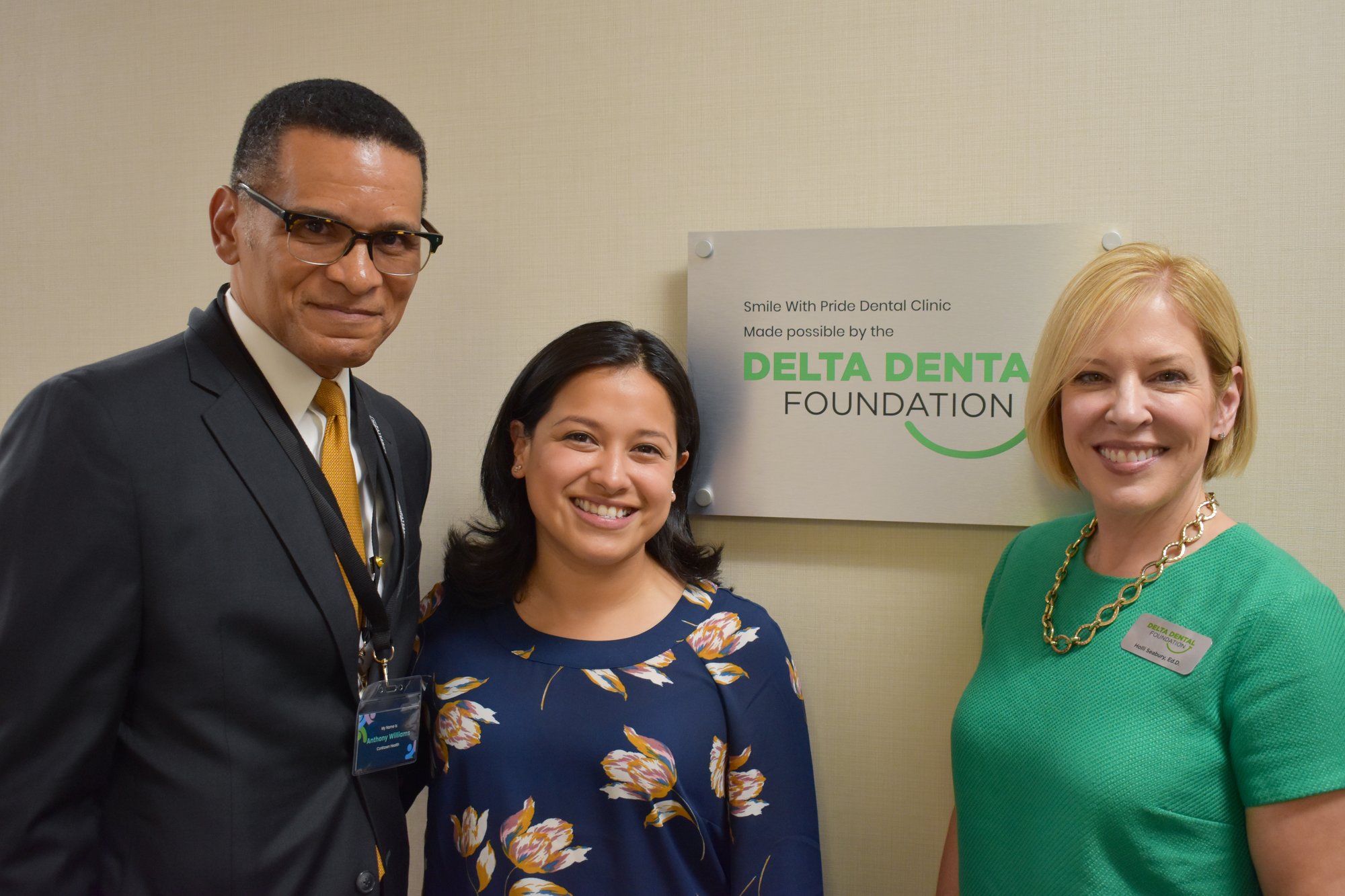 Anthony Williams, Gabriela Santiago-Romero, and Holli Seabury stand in front of a stand that reads: Smile With Pride Dental Clinic Made Possible by the Delta Dental Foundation.