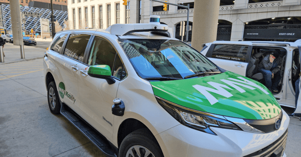 A self-driving green and white SUV with a safety driver pulls up to the curb.