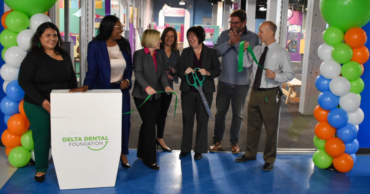 A group of people smile and laugh as they perform a "floss cutting" to celebrate a grand opening. 