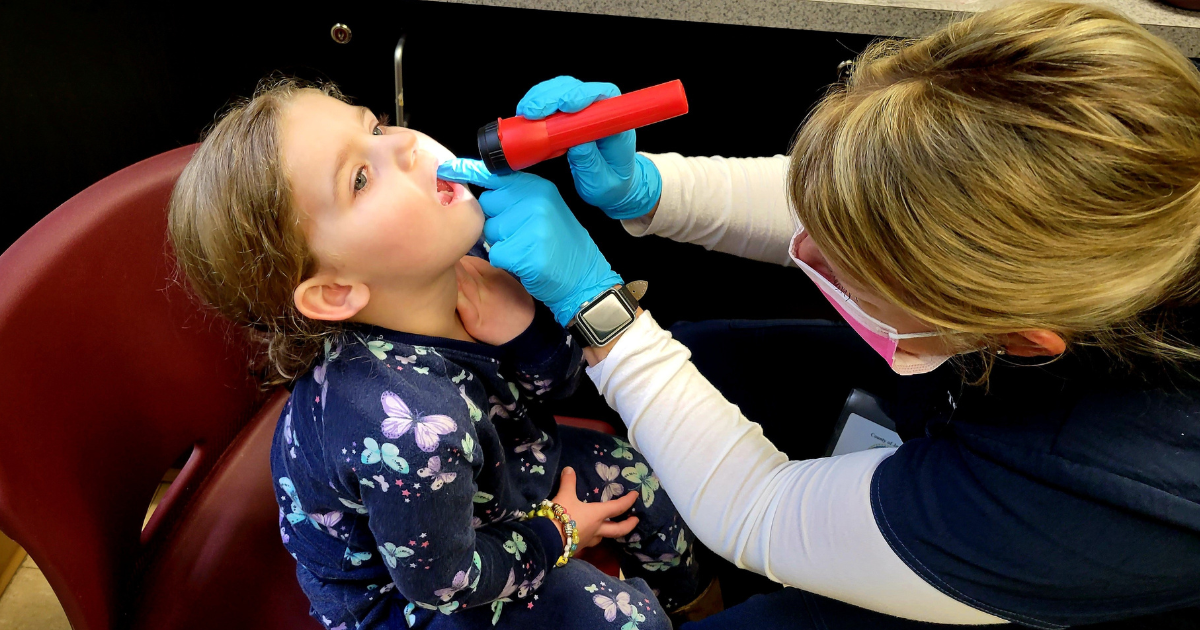 Hygienist performing a dental screening on a young girl.