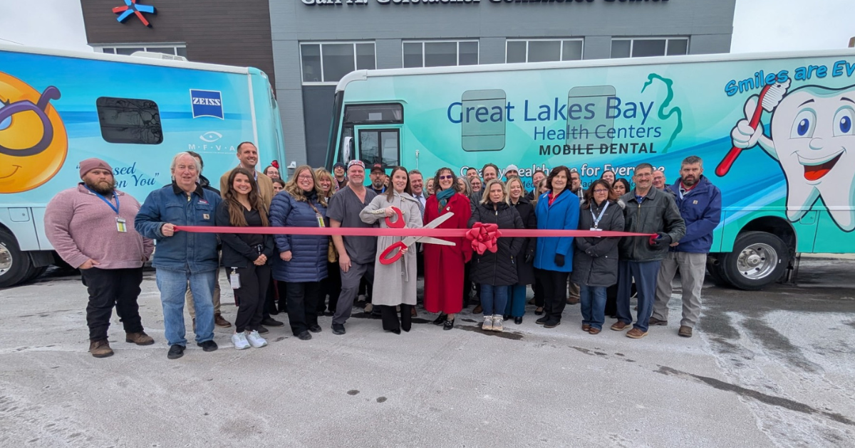 A group of people in warm winter gear hold a ribbon cutting to celebrate a new dental bus. A group of people in warm winter gear hold a ribbon cutting to celebrate a new dental bus.